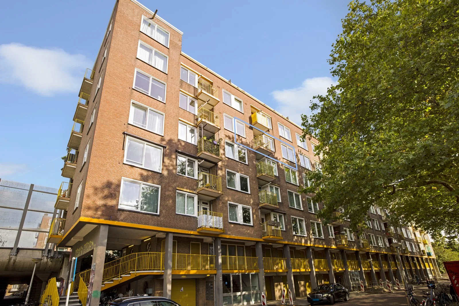 Gevel van dichtbij met gele balkonhekken en een blauwe markering rond de woning