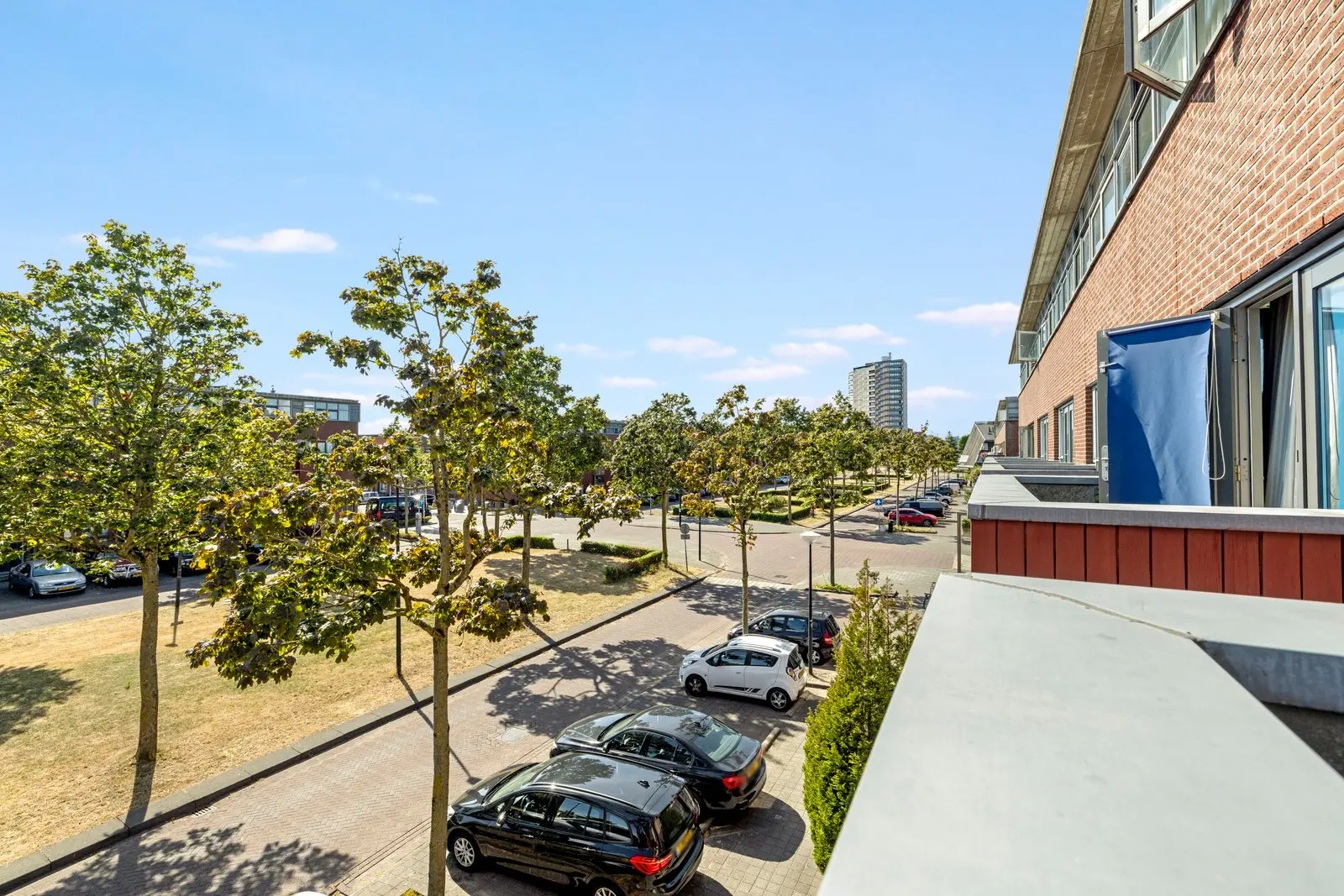 De straat voor de woning, met jonge bomen en parkeerplaatsen