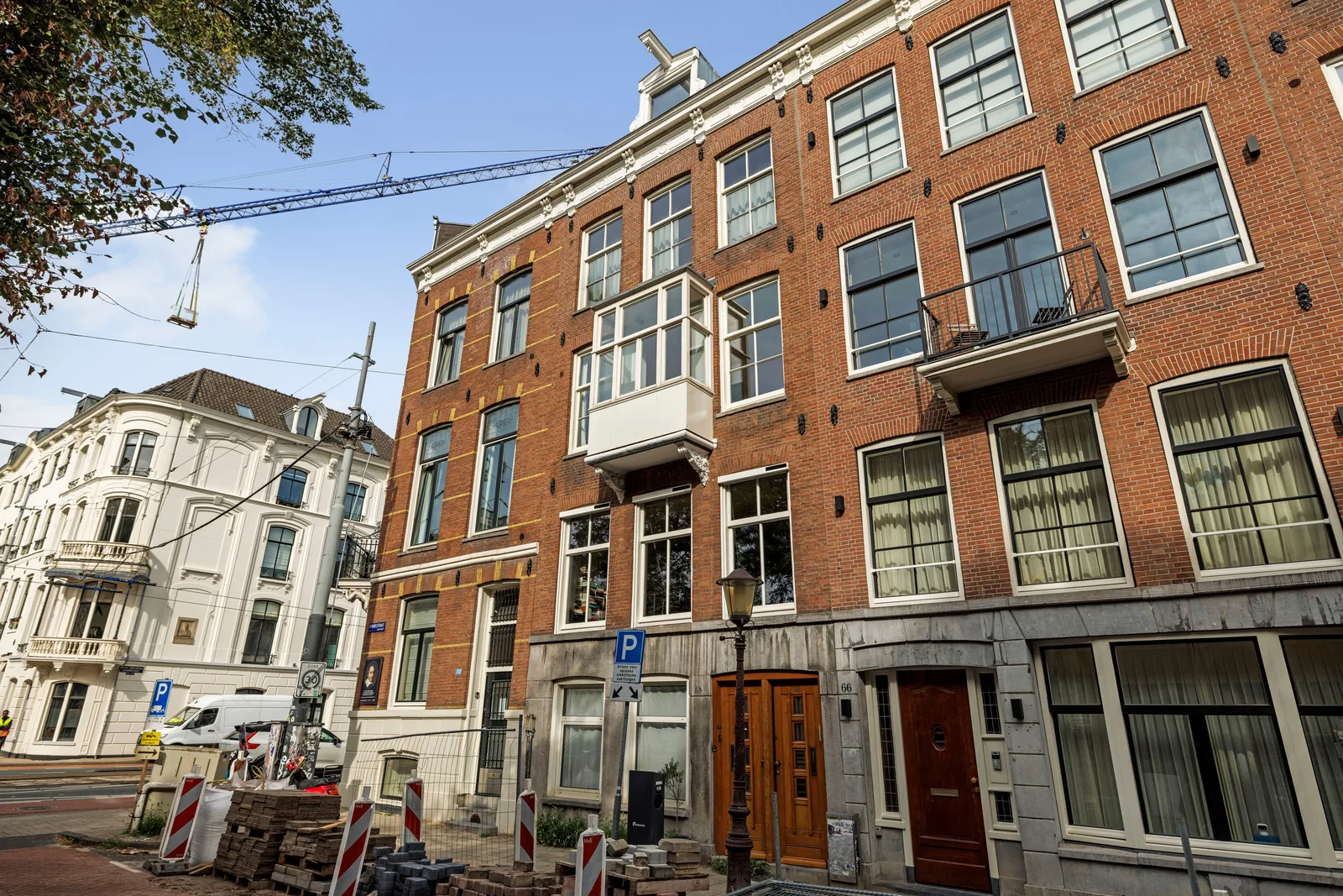 Roodbruine bakstenen gevel met witte erker, twee houten voordeuren en opgebroken stoep ervoor