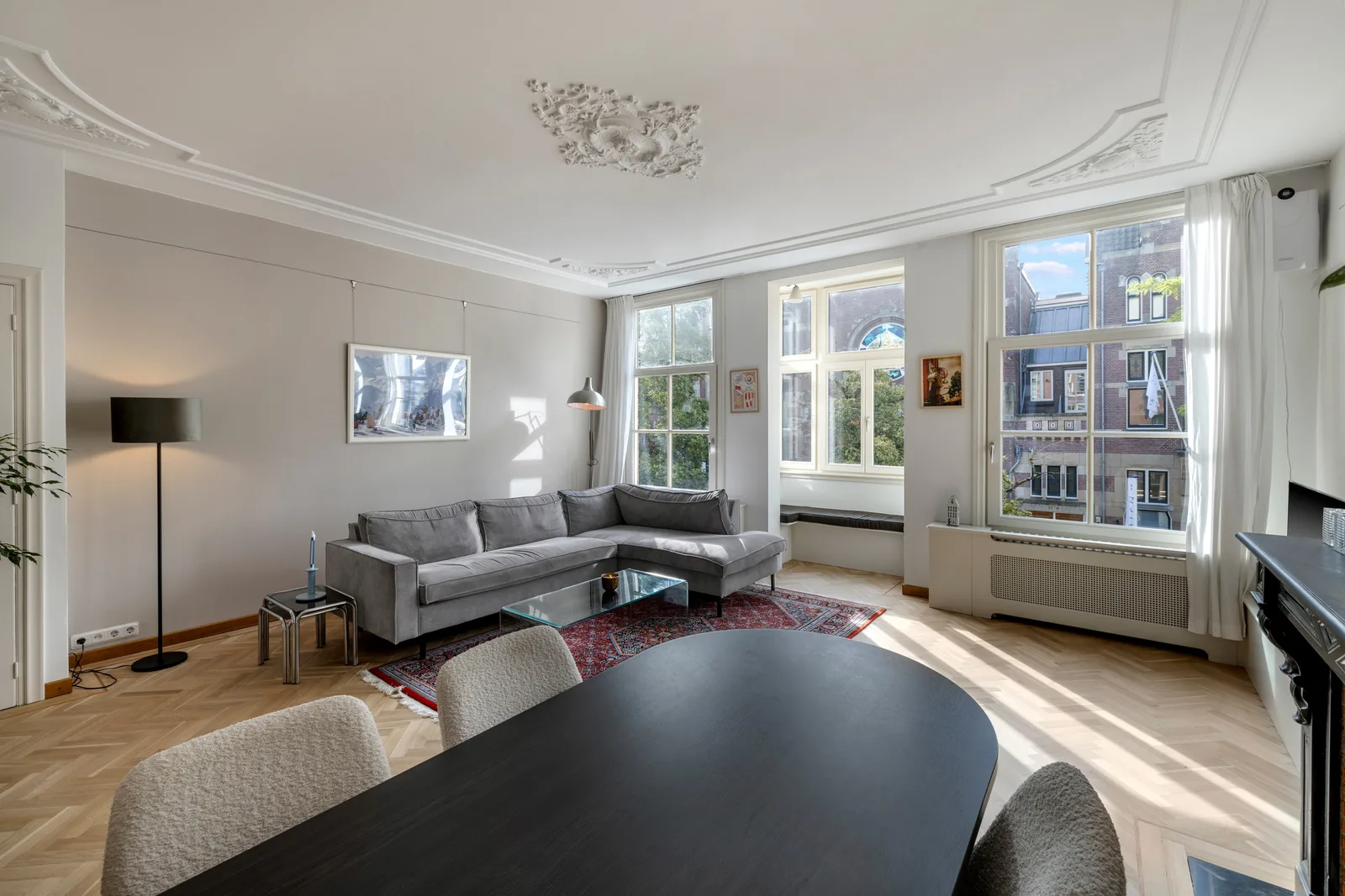 Drie hoge schuiframen met witte gordijnen, ornamenten in het plafond en een brede vensterbank