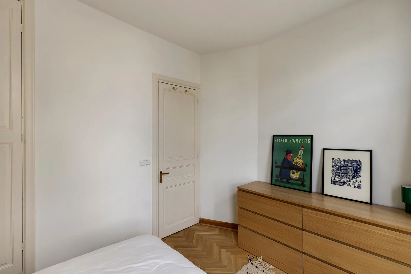 Witte paneeldeur met messing kruk, een eiken ladekast en visgraatparket in de slaapkamer
