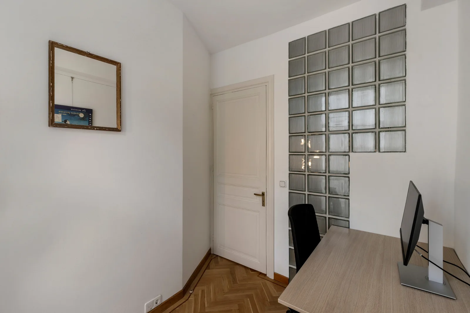 Bureau met beeldscherm voor een wand van glasbouwstenen, visgraatparket op de vloer