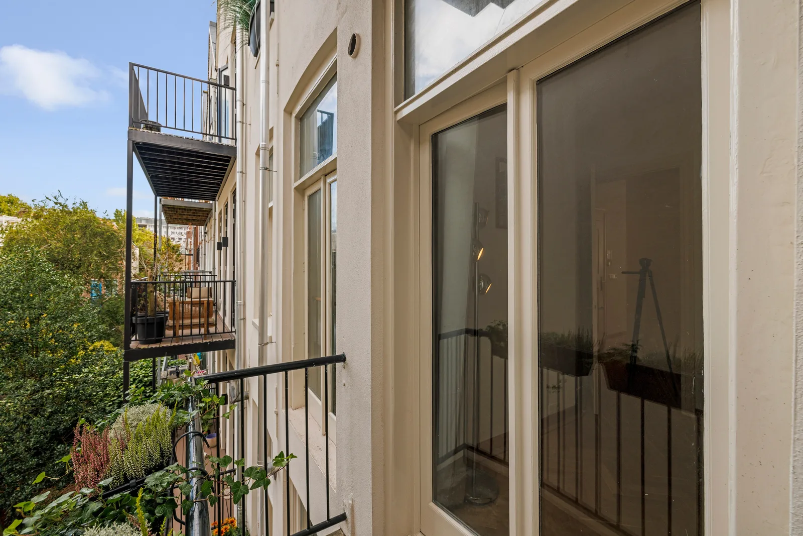 Vanaf het balkon langs de achtergevel, met houten vloer, zwart hekwerk en plantenbakken
