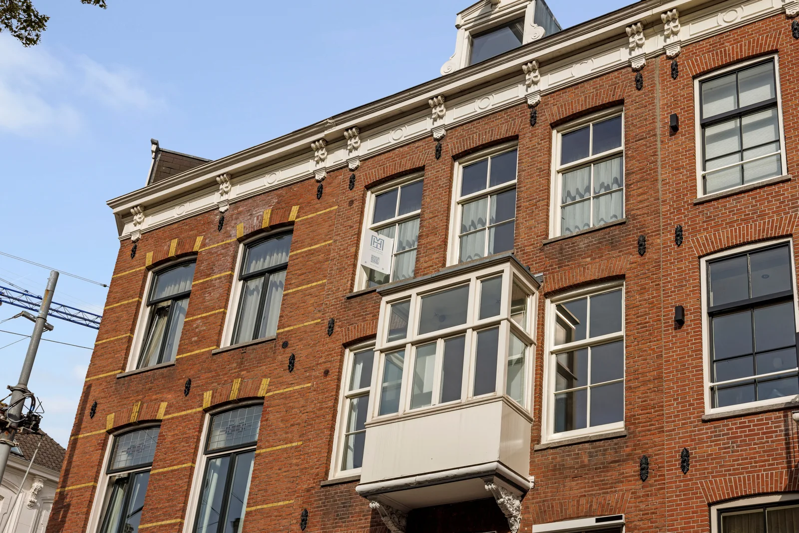 Van onderaf de rode baksteengevel met gele speklagen, witte kroonlijst en houten erker