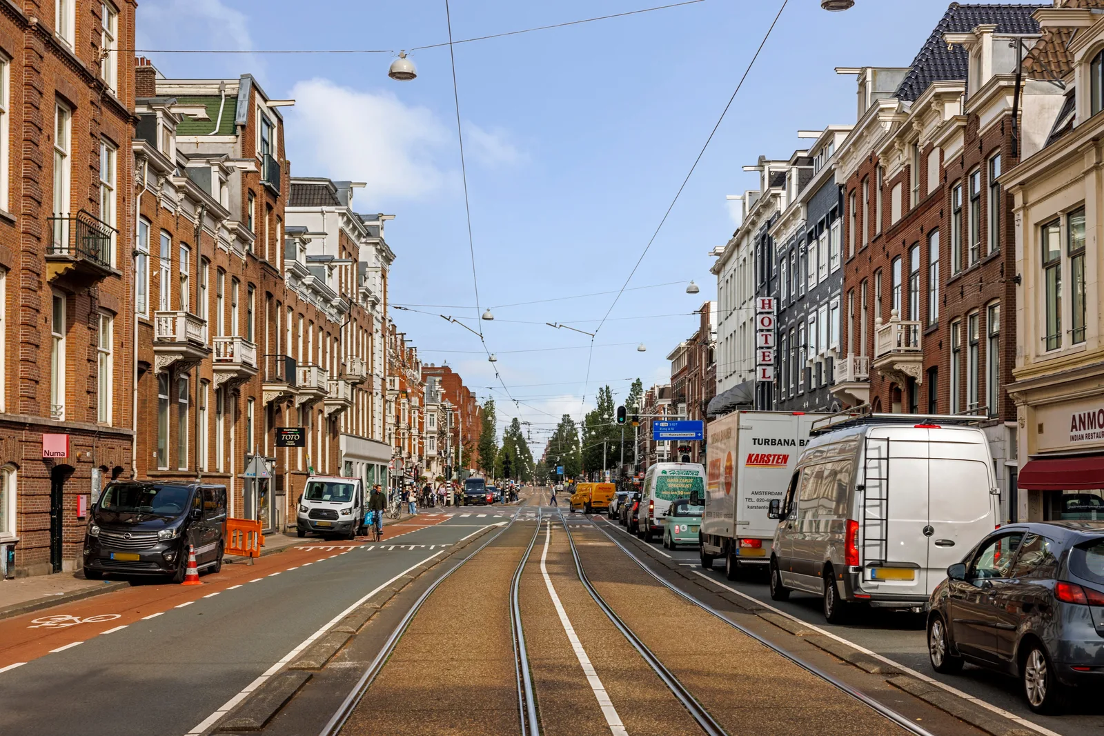 Tramrails en bovenleiding in een brede straat, winkels onder de woonlagen aan weerszijden