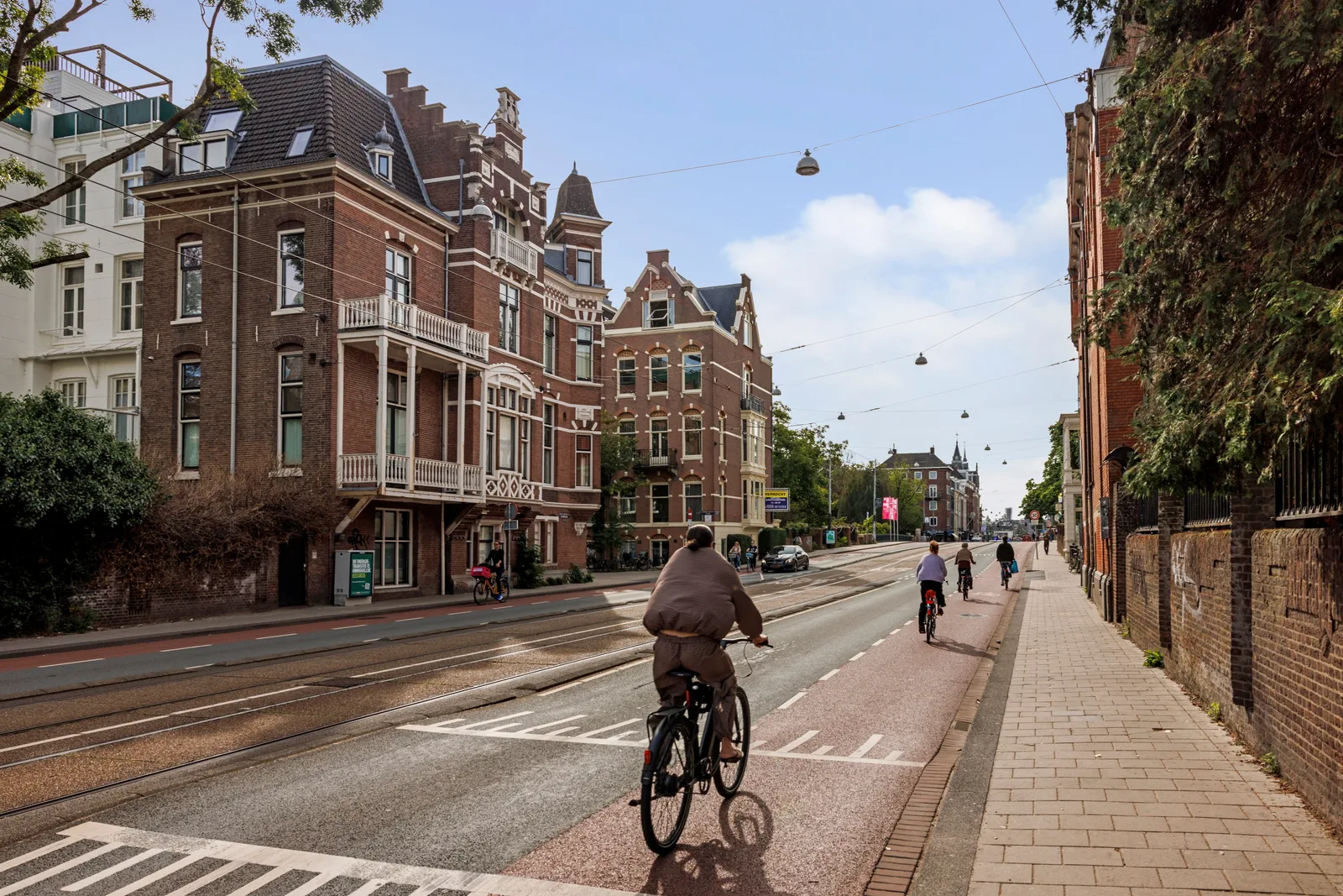 Fietsers op het rode fietspad langs de rails, aan de overkant grote herenhuizen