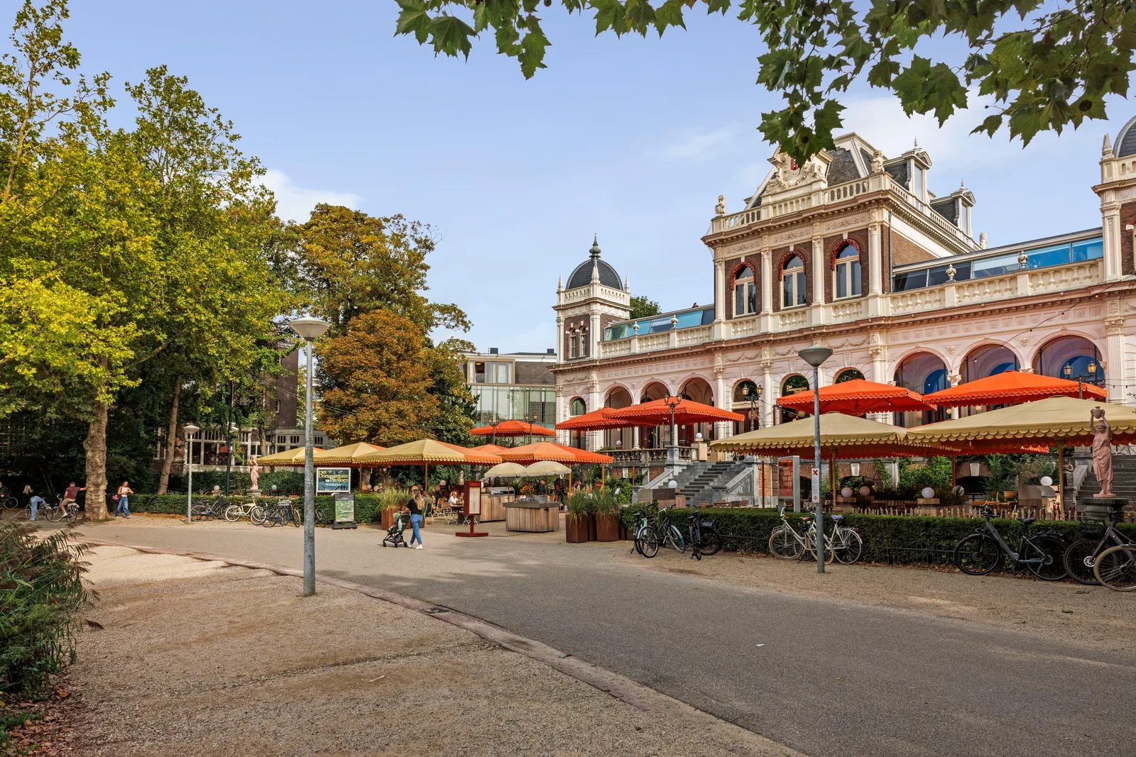 Oranje en gele parasols op het terras voor het witte paviljoen met rondbogen