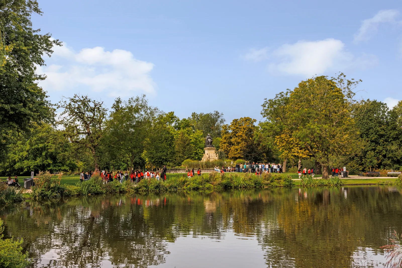 Aan de overkant van de vijver staat een standbeeld op sokkel tussen de bomen