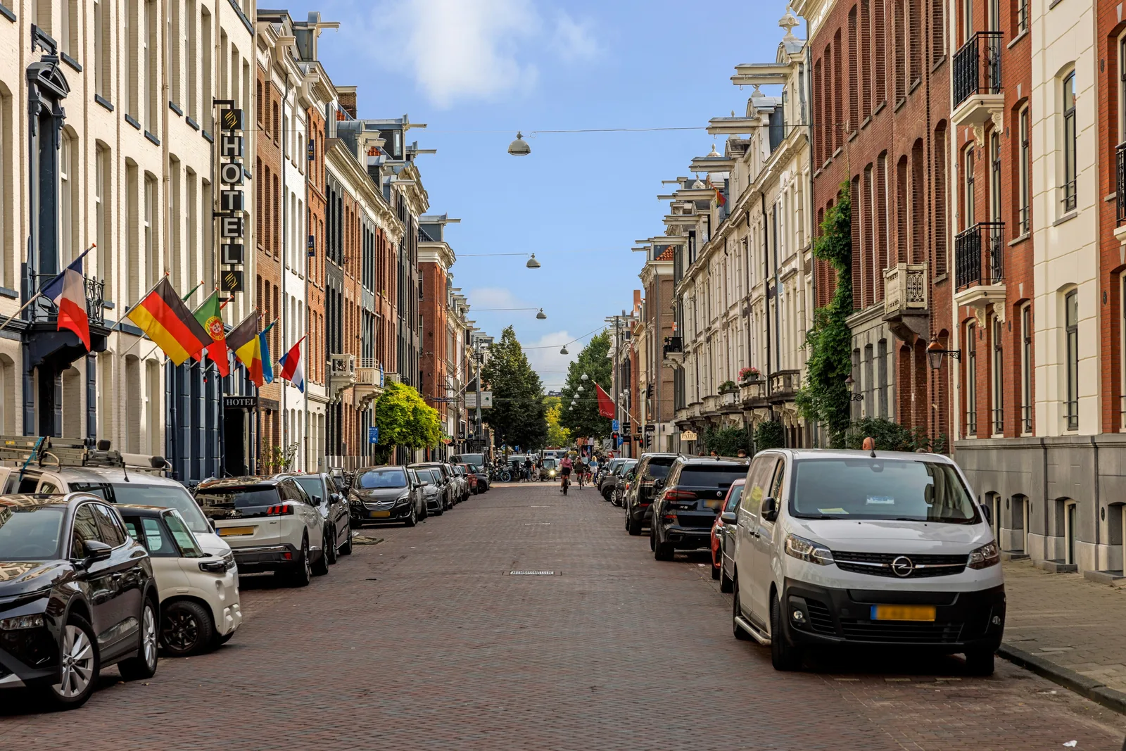 Klinkerstraat met geparkeerde auto's, historische gevels en een hotel met een rij vlaggen