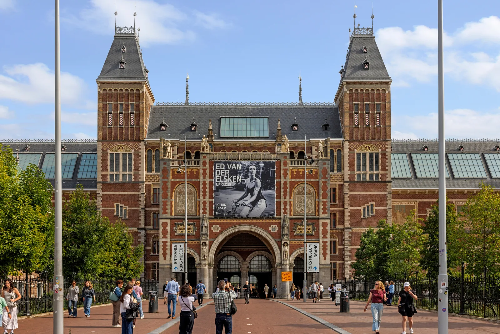 De bakstenen voorgevel van het Rijksmuseum met torens, boven de doorgang een tentoonstellingsdoek