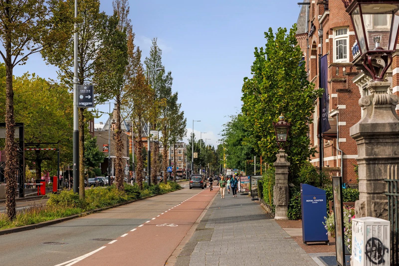 Brede laan met vrijliggend fietspad, een gietijzeren lantaarn op sokkel en wandelaars op de stoep