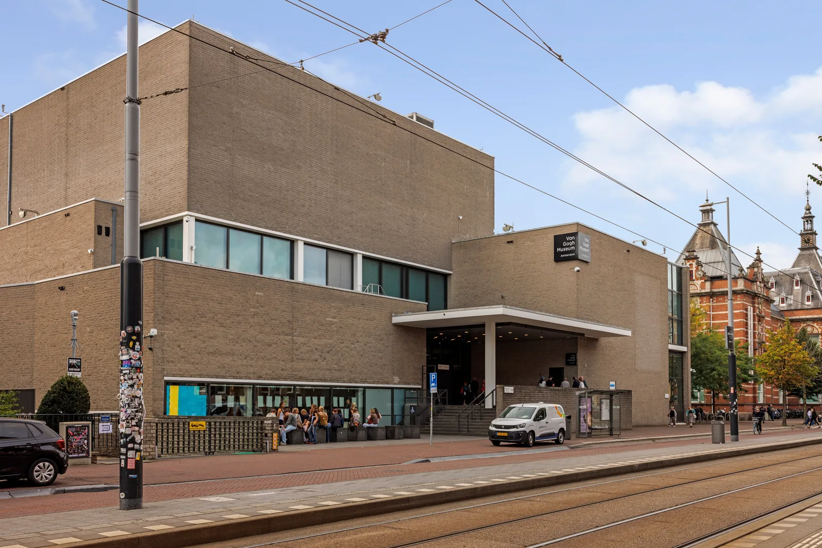 Bezoekers zitten op banken bij de ingang van het Van Gogh Museum in gele baksteen