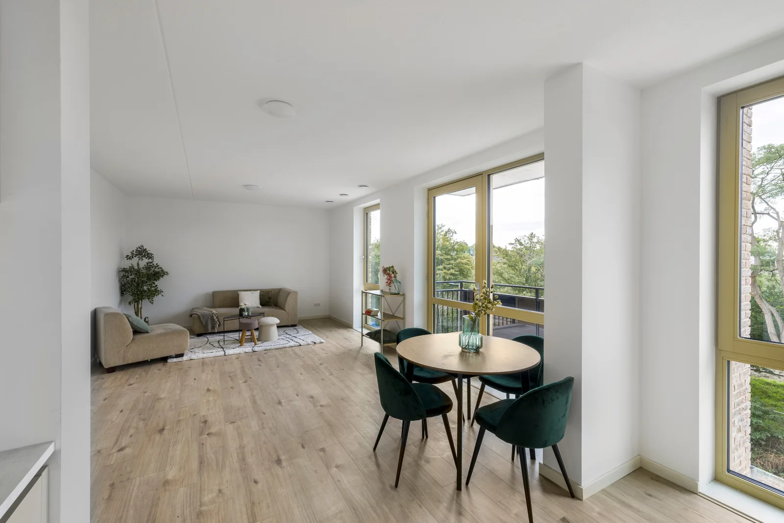 Ronde houten eettafel met vier donkergroene stoelen bij de balkondeuren, achterin de zithoek