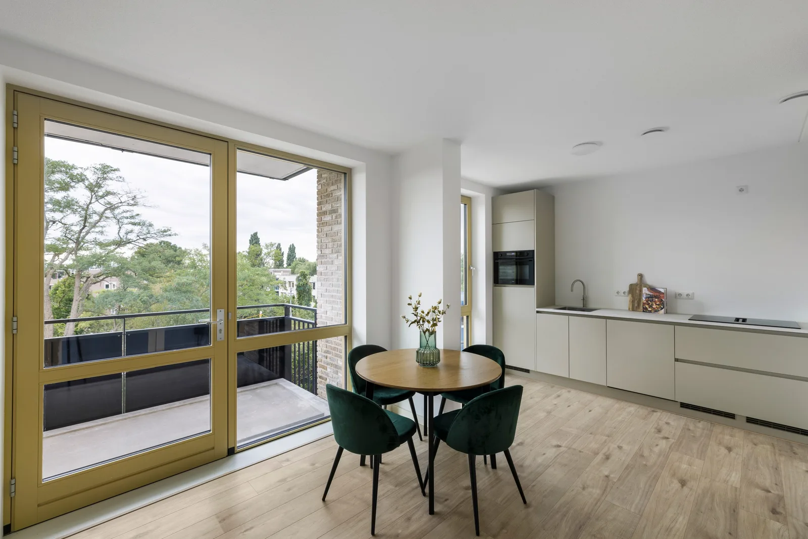 Ronde houten eettafel met vier donkergroene stoelen bij de glazen balkondeur, keuken rechts