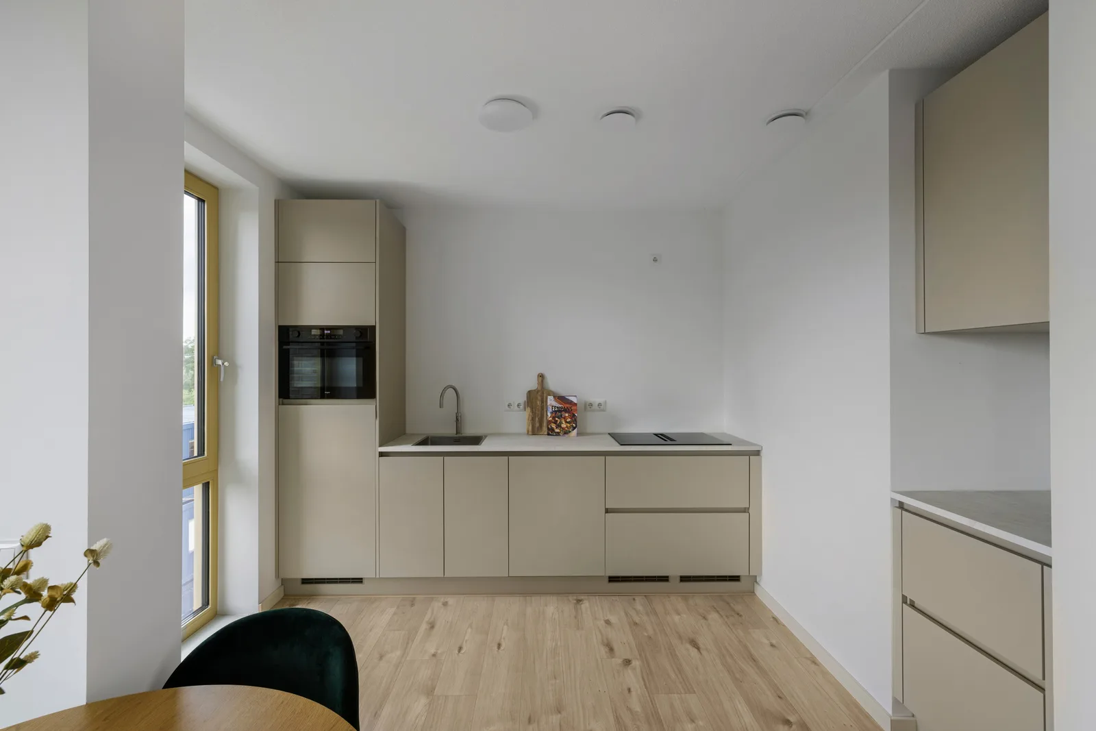 Beige keukenopstelling met rvs spoelbak, zwarte kookplaat en een hoge kast met inbouwoven