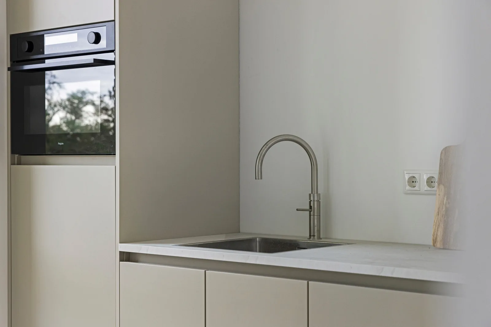 Beige greeploze keukenkasten met ingebouwde oven, stalen kraan en verzonken spoelbak in het wit gemarmerde blad