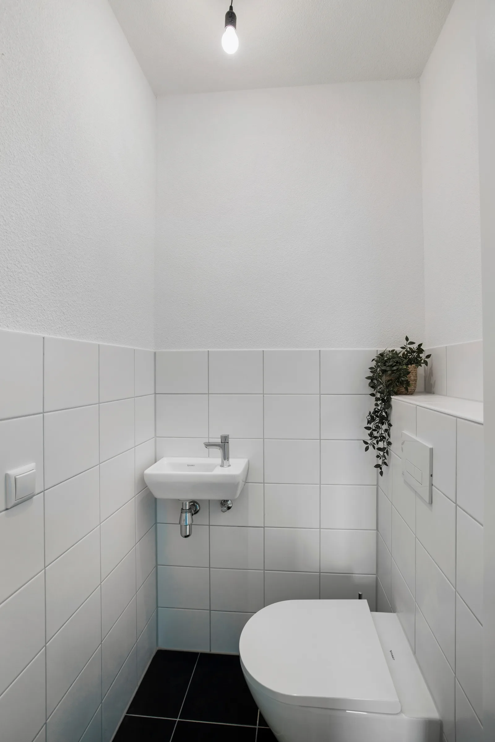 Toilet met witte wandtegels, zwarte vloertegels, wit closet en kleine fontein met chromen kraan