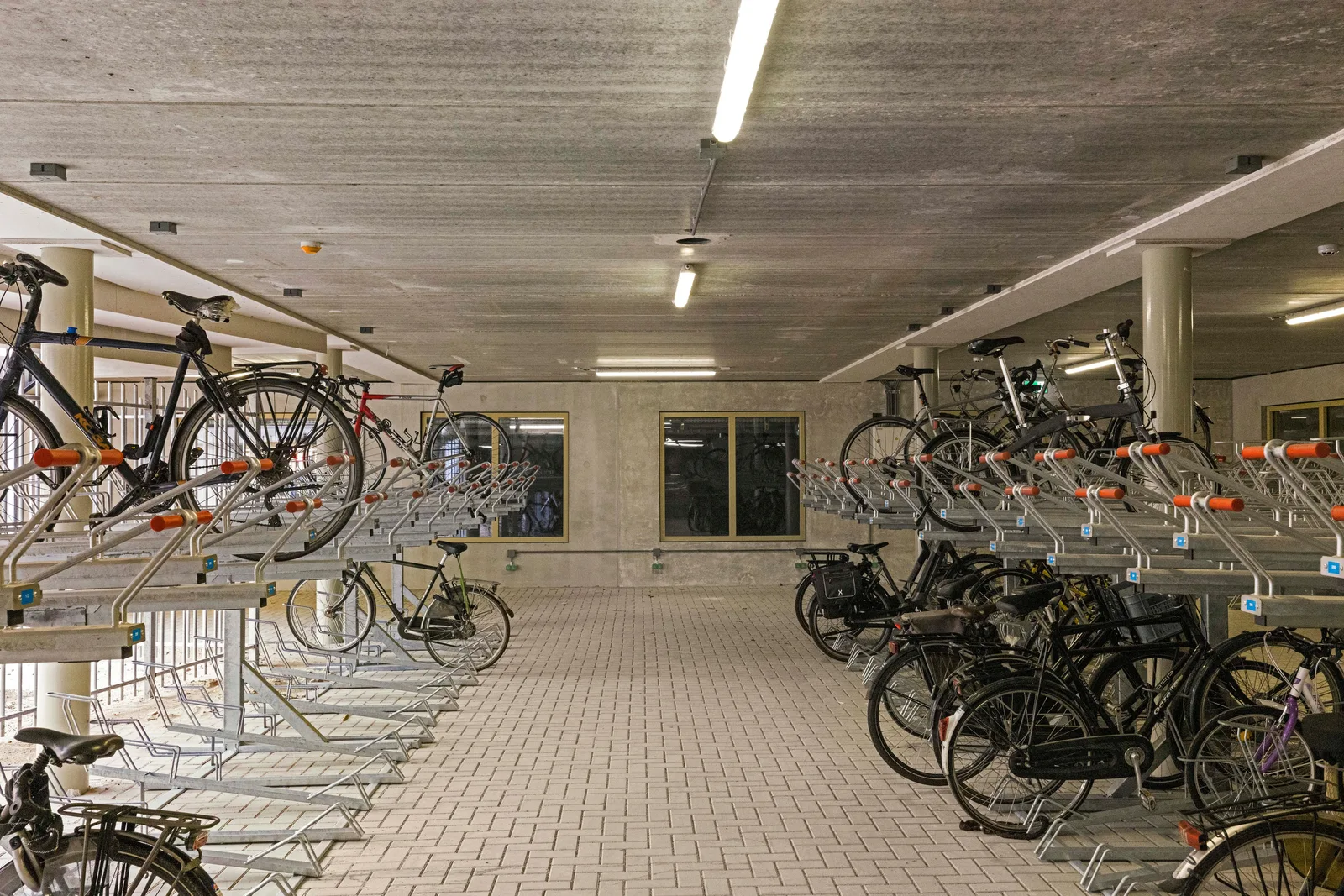 Looppad van lichte klinkers tussen dubbellaagse fietsrekken met oranje uiteinden, fietsen op beide lagen