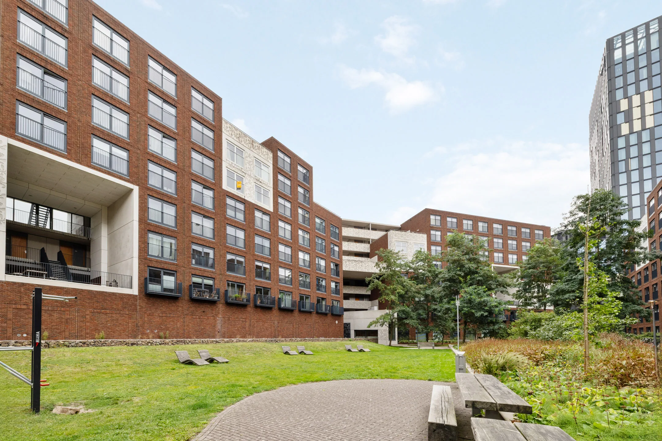 Het groene binnenhof van het wooncomplex, met ligbanken in het gras en woonblokken eromheen