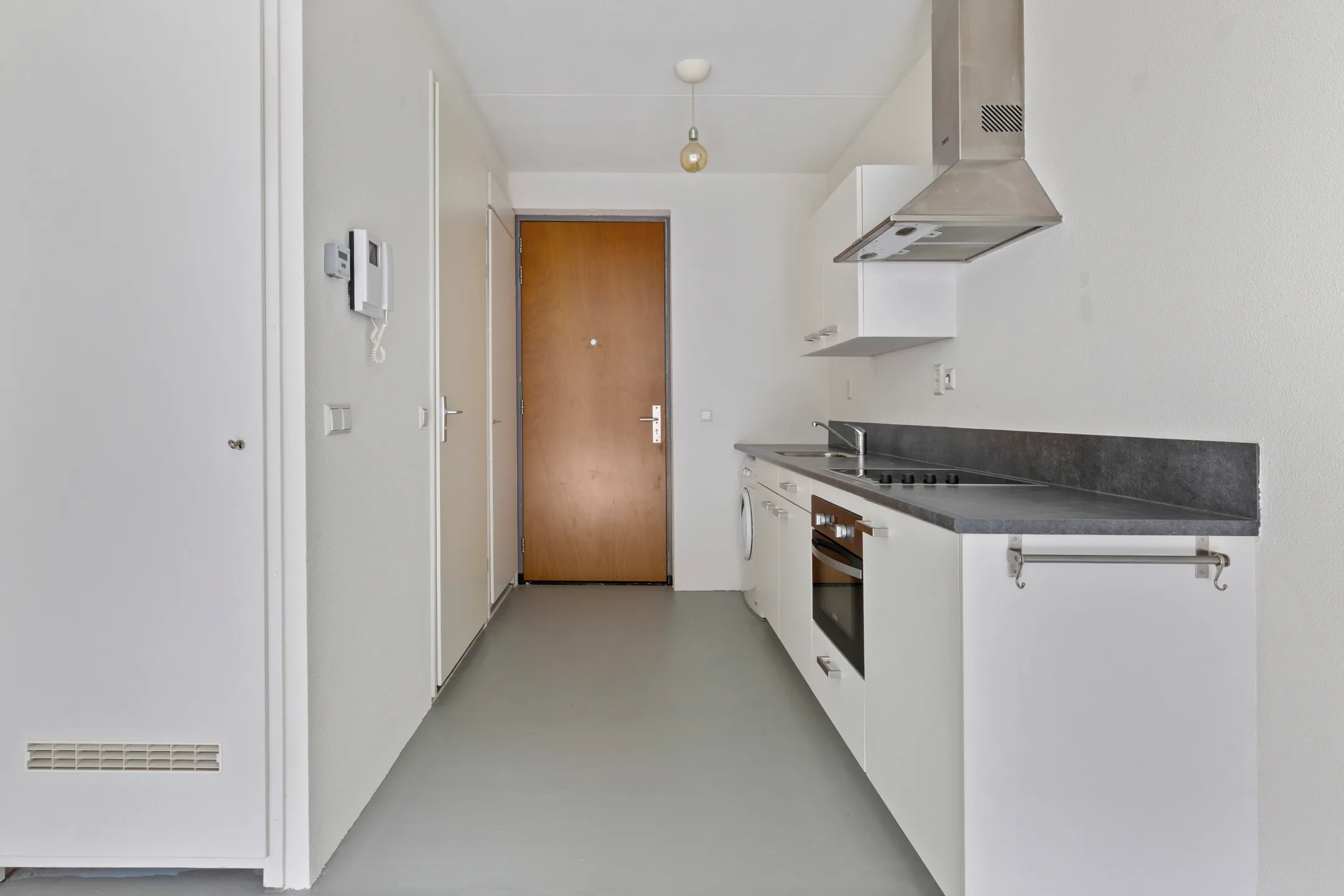 Hal van het appartement met het keukenblok langs de wand, de intercom en de voordeur