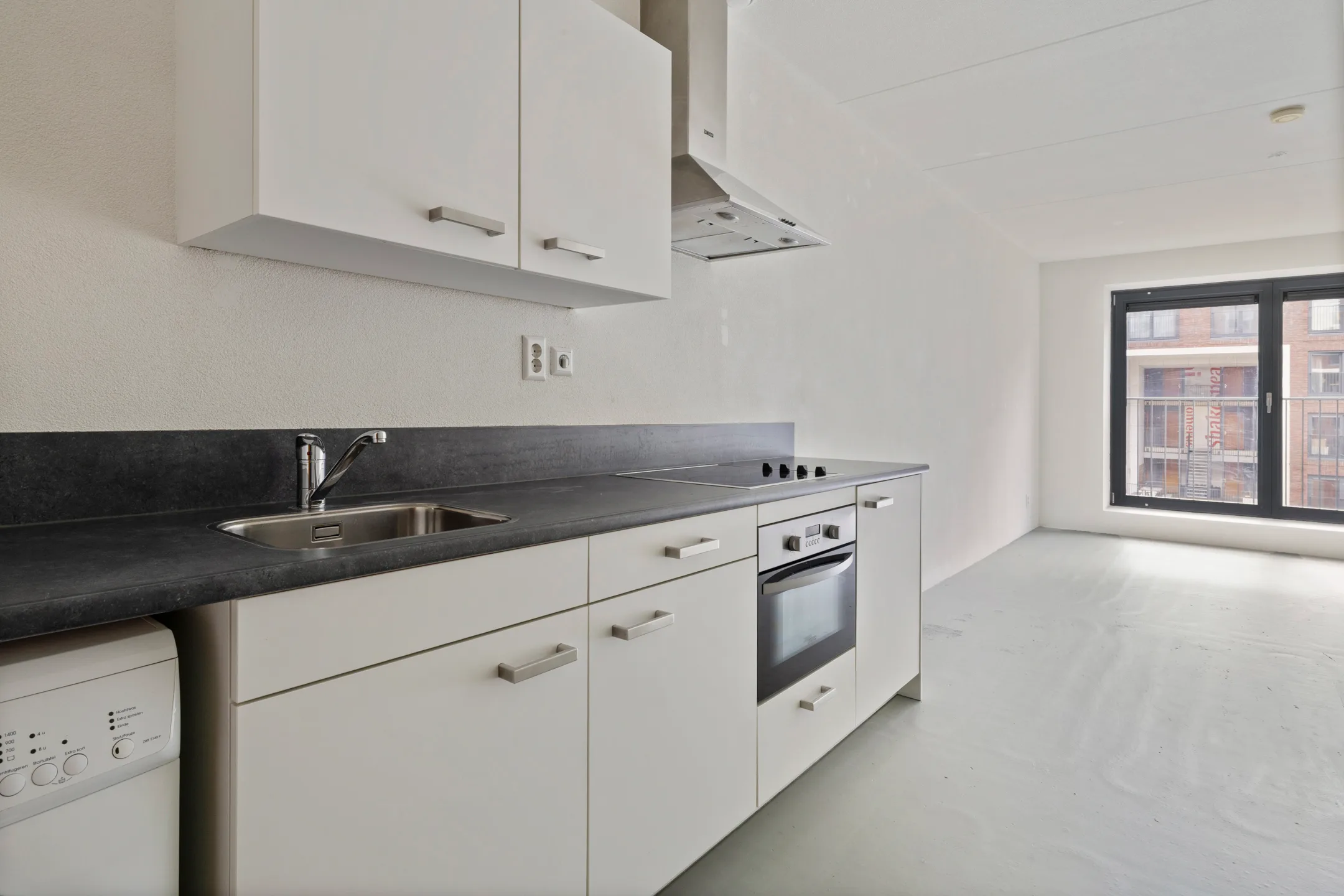 Keuken met spoelbak, kookplaat, oven en vaatwasser, met doorkijk naar het raam