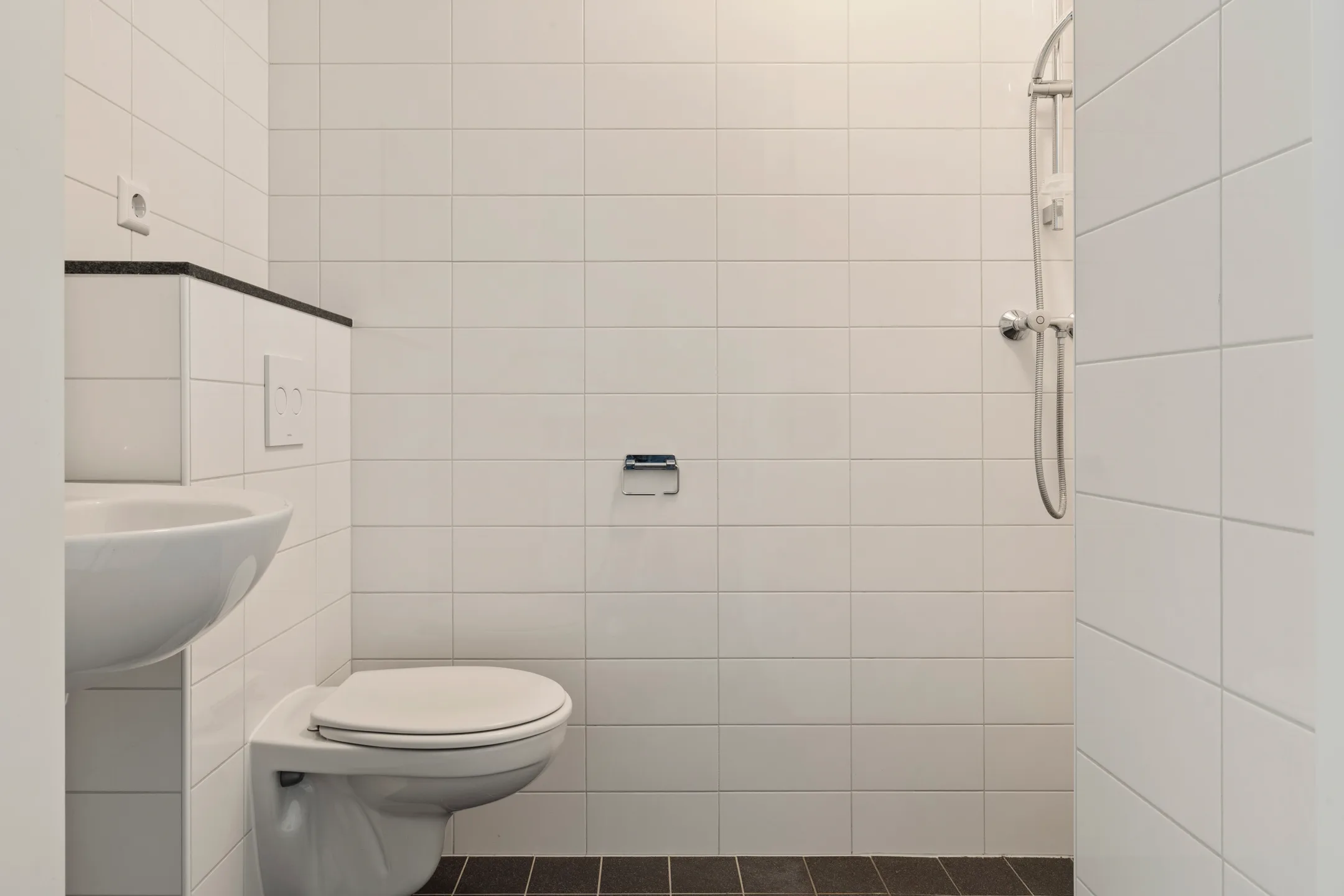 Badkamer met wastafel, hangend toilet en een douche zonder wand