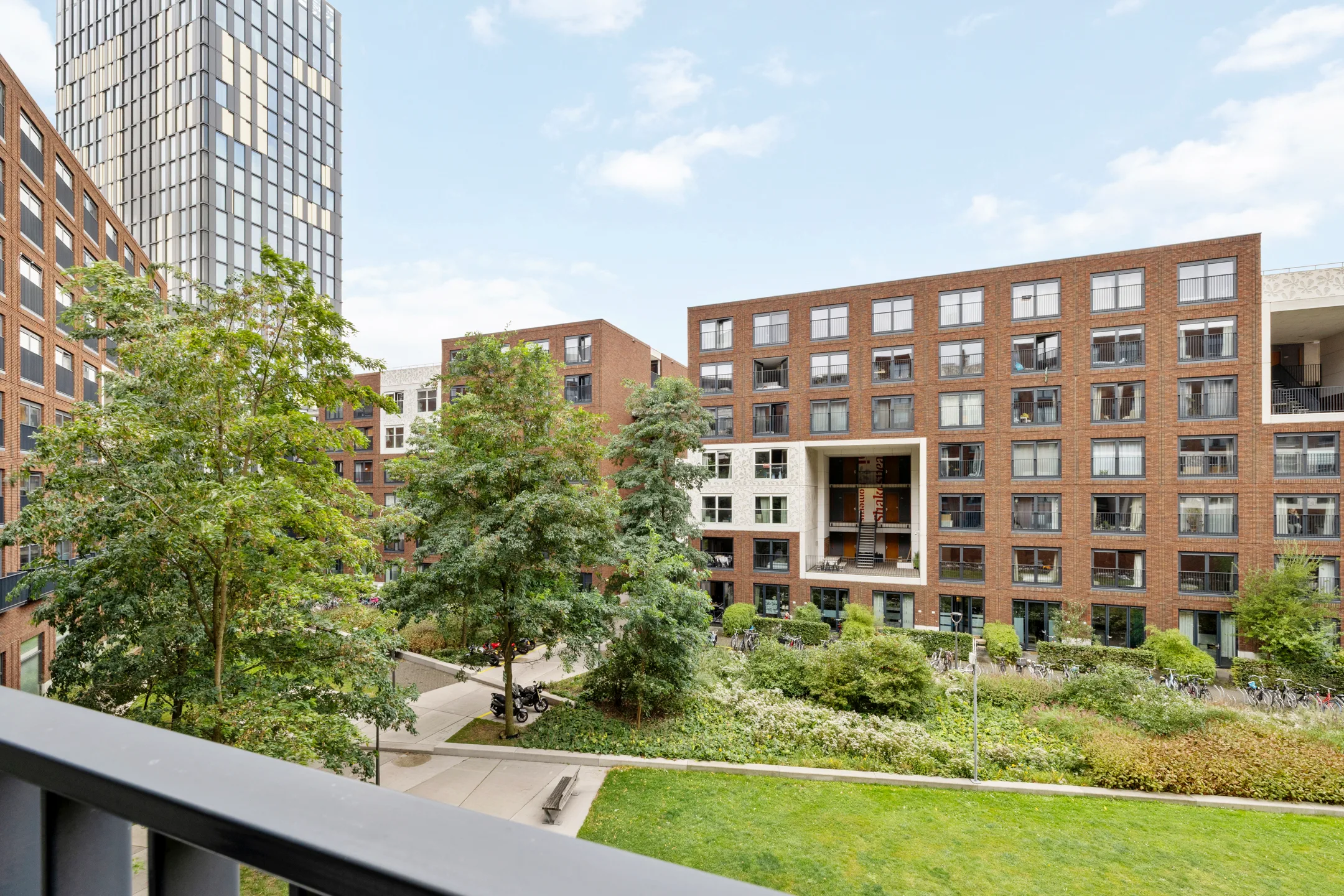 Uitzicht vanaf het balkon in de andere richting, met bomen op het binnenterrein en een woontoren erachter
