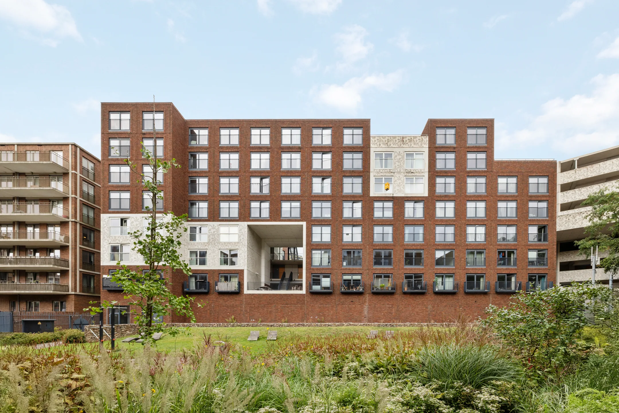 Rechte opname van de bakstenen gevel van het wooncomplex aan de Welnastraat in Amsterdam, gezien vanaf de beplante groenstrook