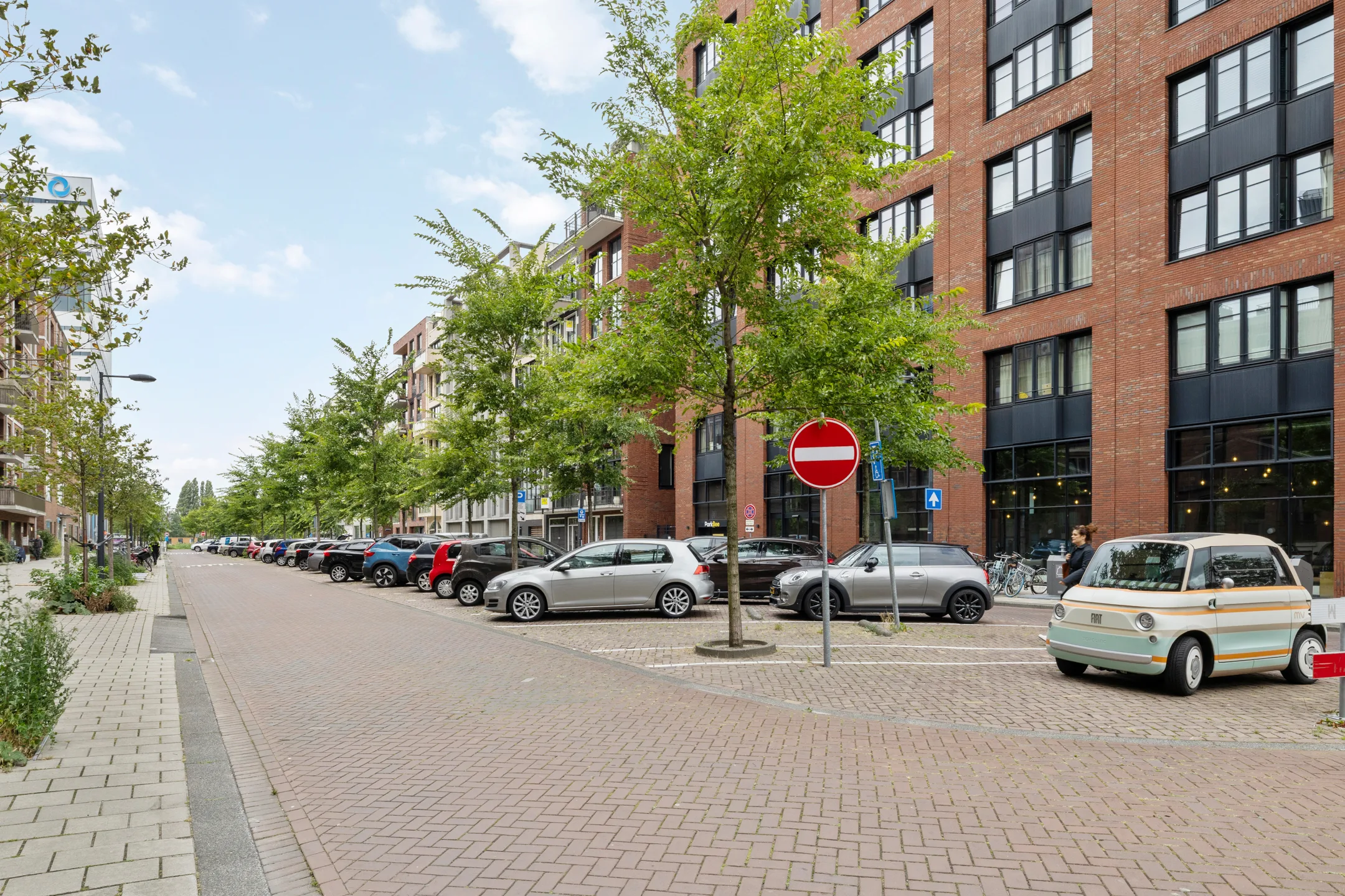 De straat langs het complex, met geparkeerde auto's en jonge bomen